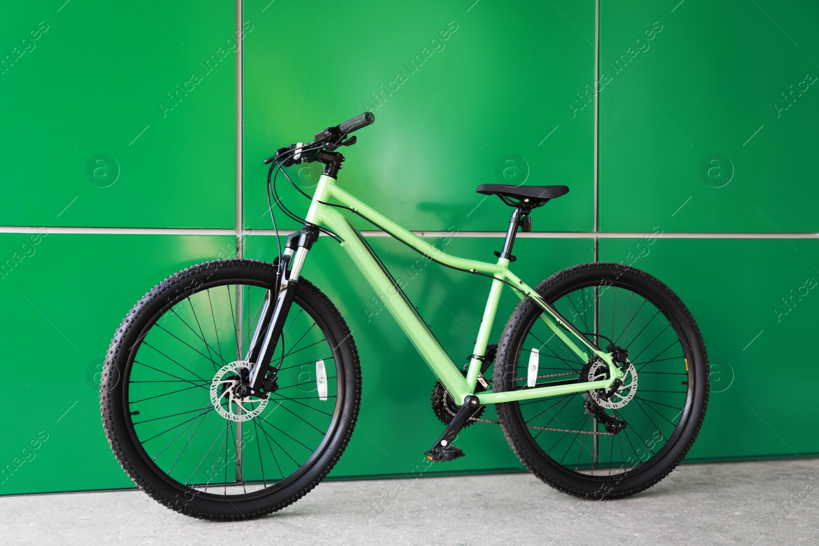 Photo of New modern color bicycle near green wall outdoors