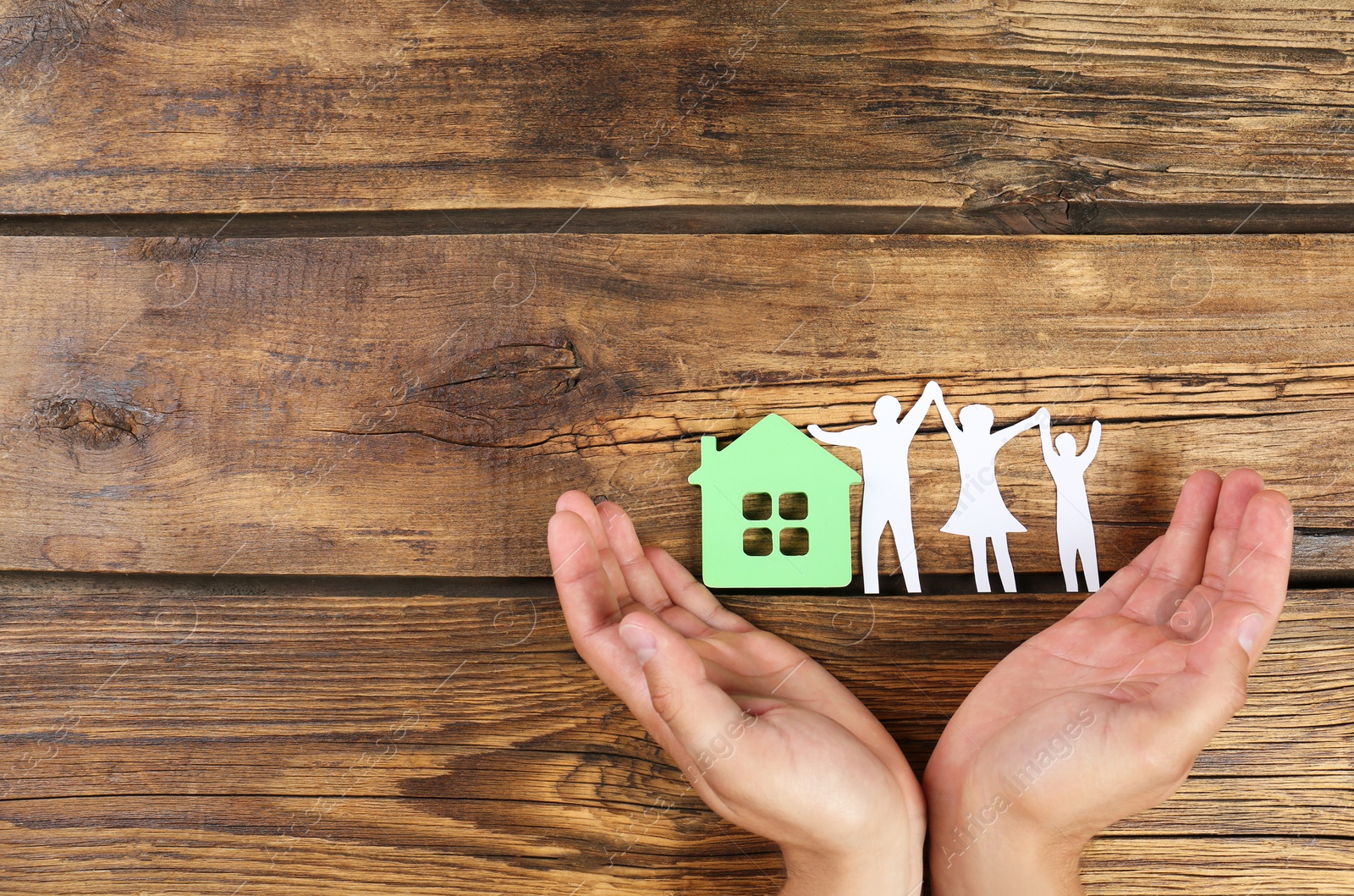 Photo of Young man protecting family figure and house model with his hands on wooden background, top view. Space for text