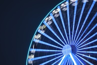 Big glowing Ferris wheel against dark blue sky at night. Space for text