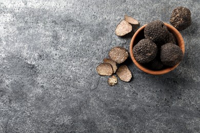 Photo of Black truffles with wooden bowl on grey table, flat lay. Space for text