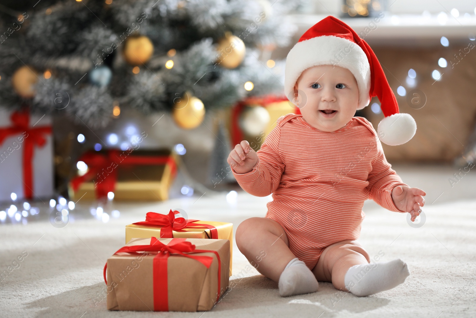 Photo of Little baby wearing Santa hat on floor indoors. First Christmas