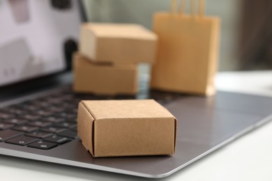 Photo of Online store. Laptop and mini parcel on white table, closeup