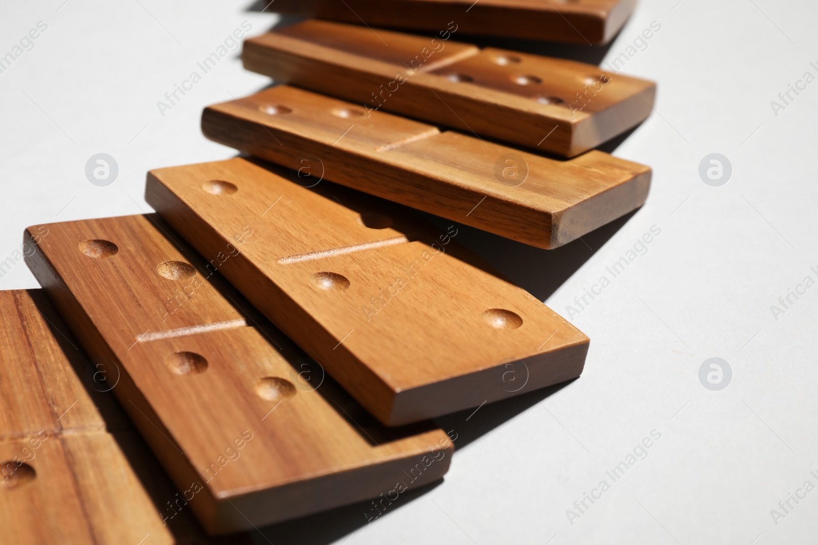 Photo of Fallen wooden domino tiles on light grey background, closeup