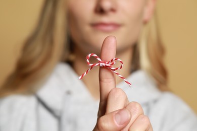 Photo of Woman showing index finger with tied bow as reminder against light brown background, focus on hand