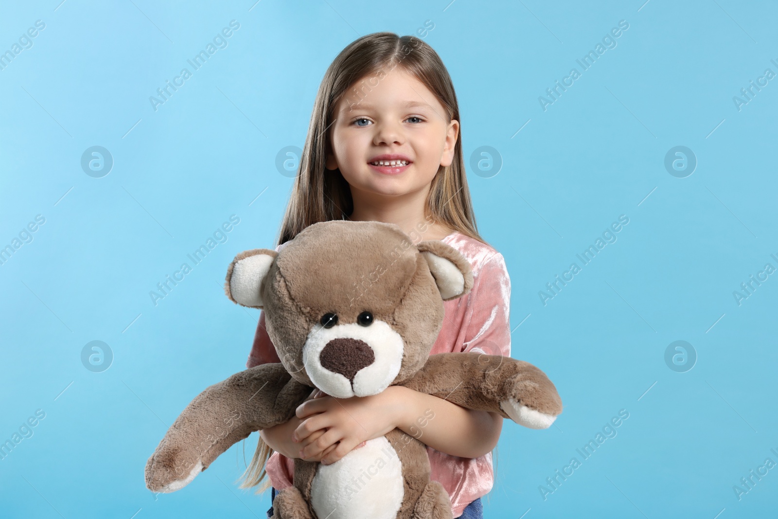 Photo of Cute little girl with teddy bear on light blue background