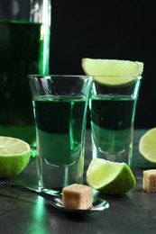 Photo of Absinthe in shot glasses, spoon, brown sugar cubes and lime on gray textured table, closeup. Alcoholic drink