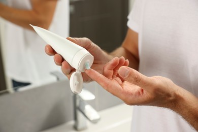 Photo of Handsome man applying cream in bathroom, closeup