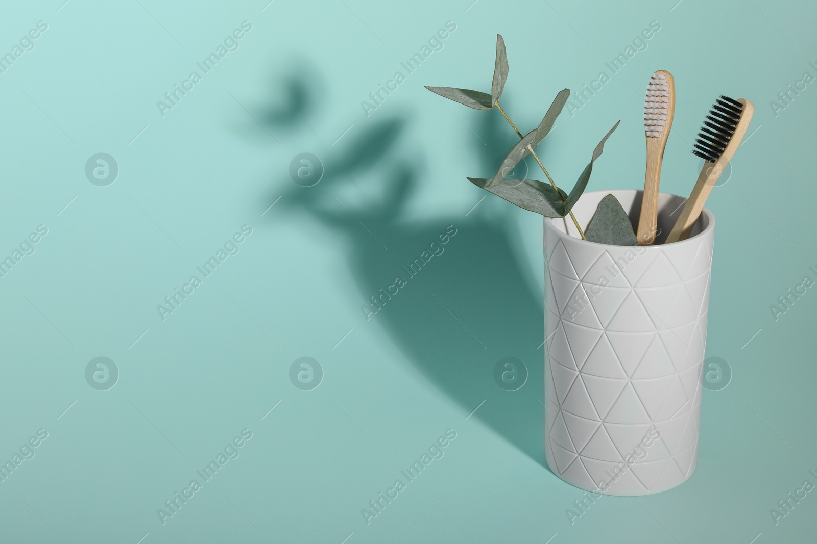 Photo of Bamboo toothbrushes and eucalyptus branch in holder on turquoise background, space for text