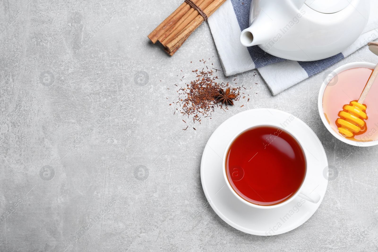 Photo of Freshly brewed rooibos tea, scattered dry leaves, honey and spices on grey table, flat lay. Space for text