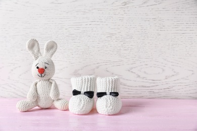 Handmade baby booties and stuffed rabbit on table against wooden background