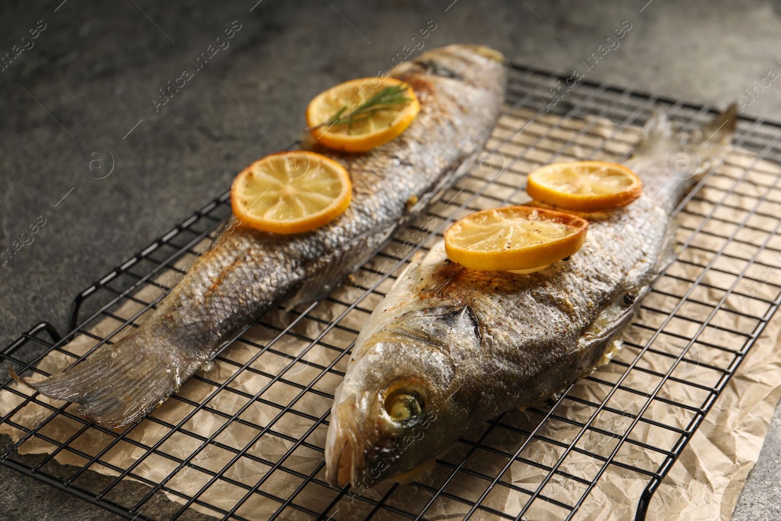 Photo of Baked fish with lemon on grey textured table, closeup