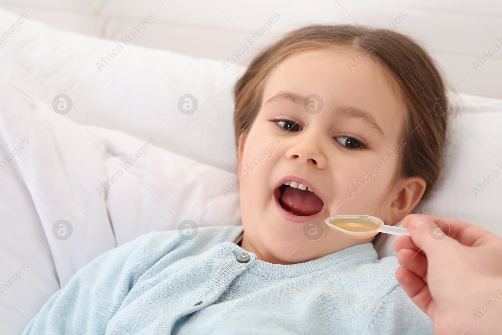 Photo of Mother giving cough syrup to her daughter in bedroom