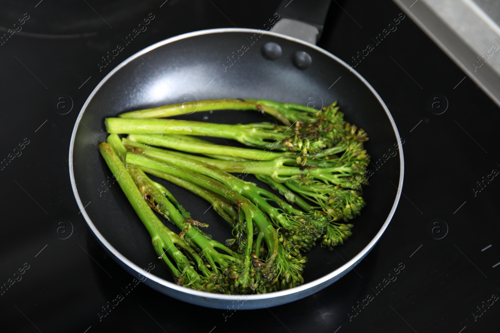 Photo of Frying pan with tasty cooked broccolini on cooktop, closeup