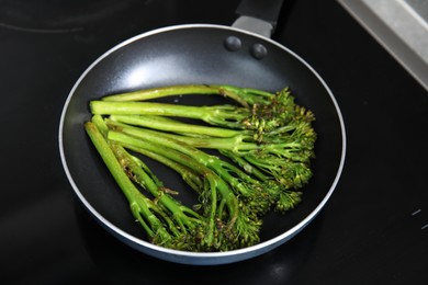 Frying pan with tasty cooked broccolini on cooktop, closeup