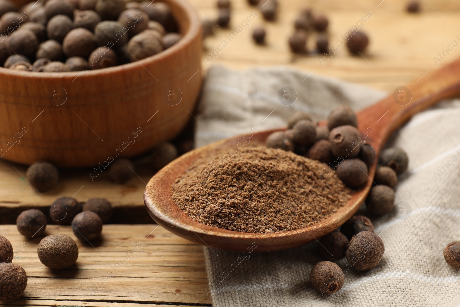 Photo of Aromatic allspice pepper grains, powder and spoon on wooden table, closeup