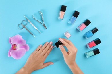 Woman applying nail polish on color background, above view