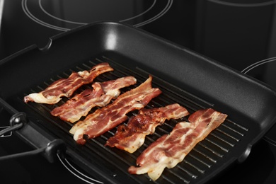 Photo of Slices of tasty fried bacon in grill pan indoors