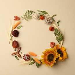 Photo of Dried flowers and leaves arranged in shape of wreath on beige background, flat lay with space for text. Autumnal aesthetic