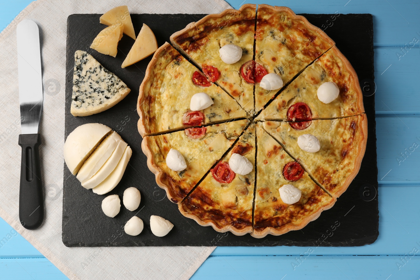 Photo of Delicious homemade cheese quiche and ingredients on light blue wooden table, flat lay