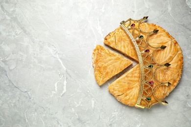 Photo of Traditional galette des Rois with decorative crown on grey marble table, flat lay. Space for text