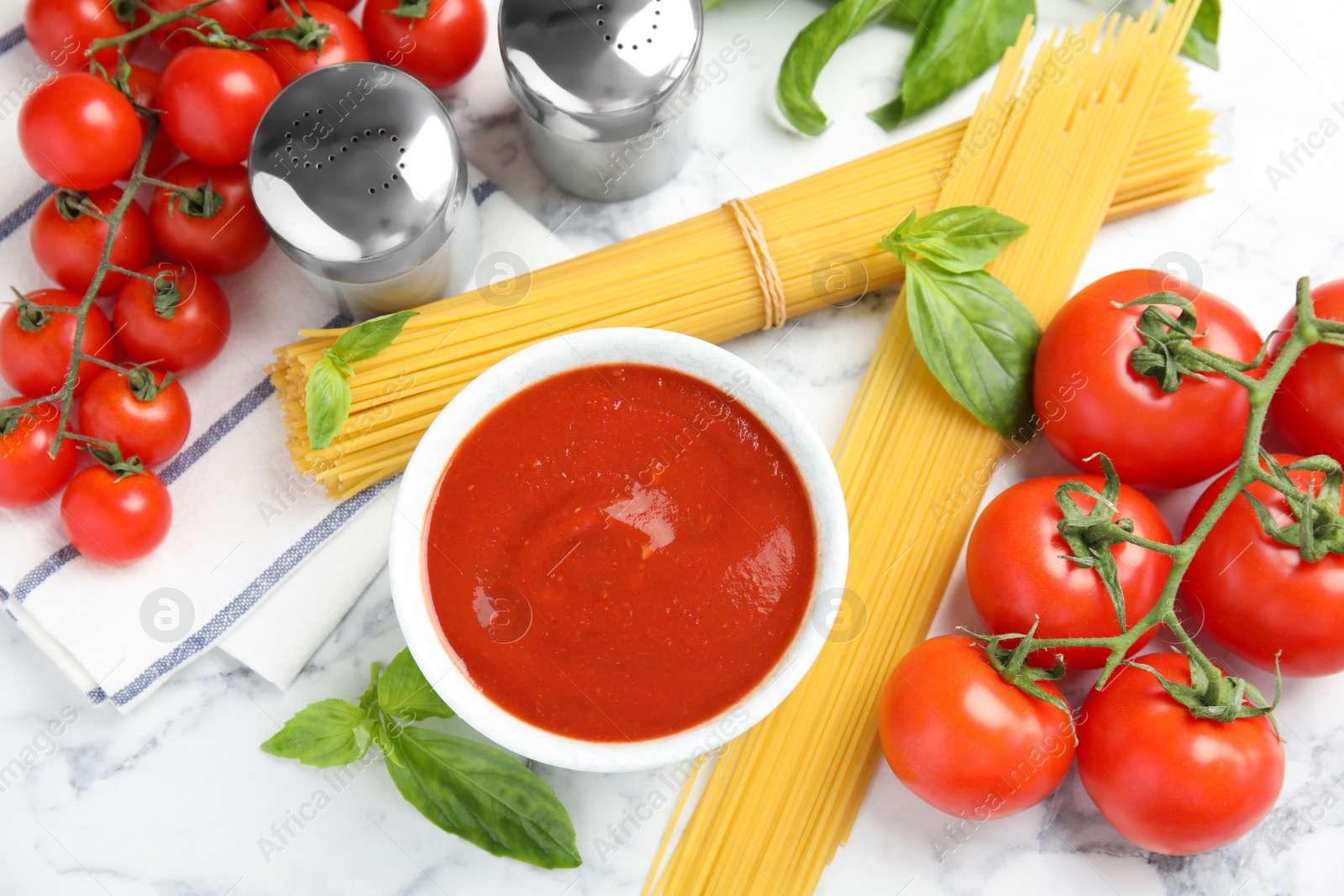 Photo of Flat lay composition with bowl of sauce, pasta and tomatoes on marble table