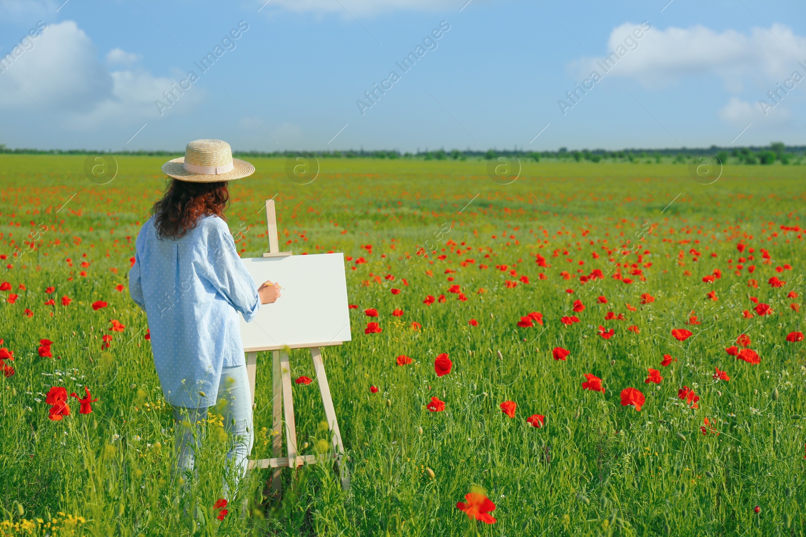 Photo of Woman painting on easel in beautiful poppy field