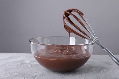 Photo of Bowl and whisk with chocolate cream on table against grey background