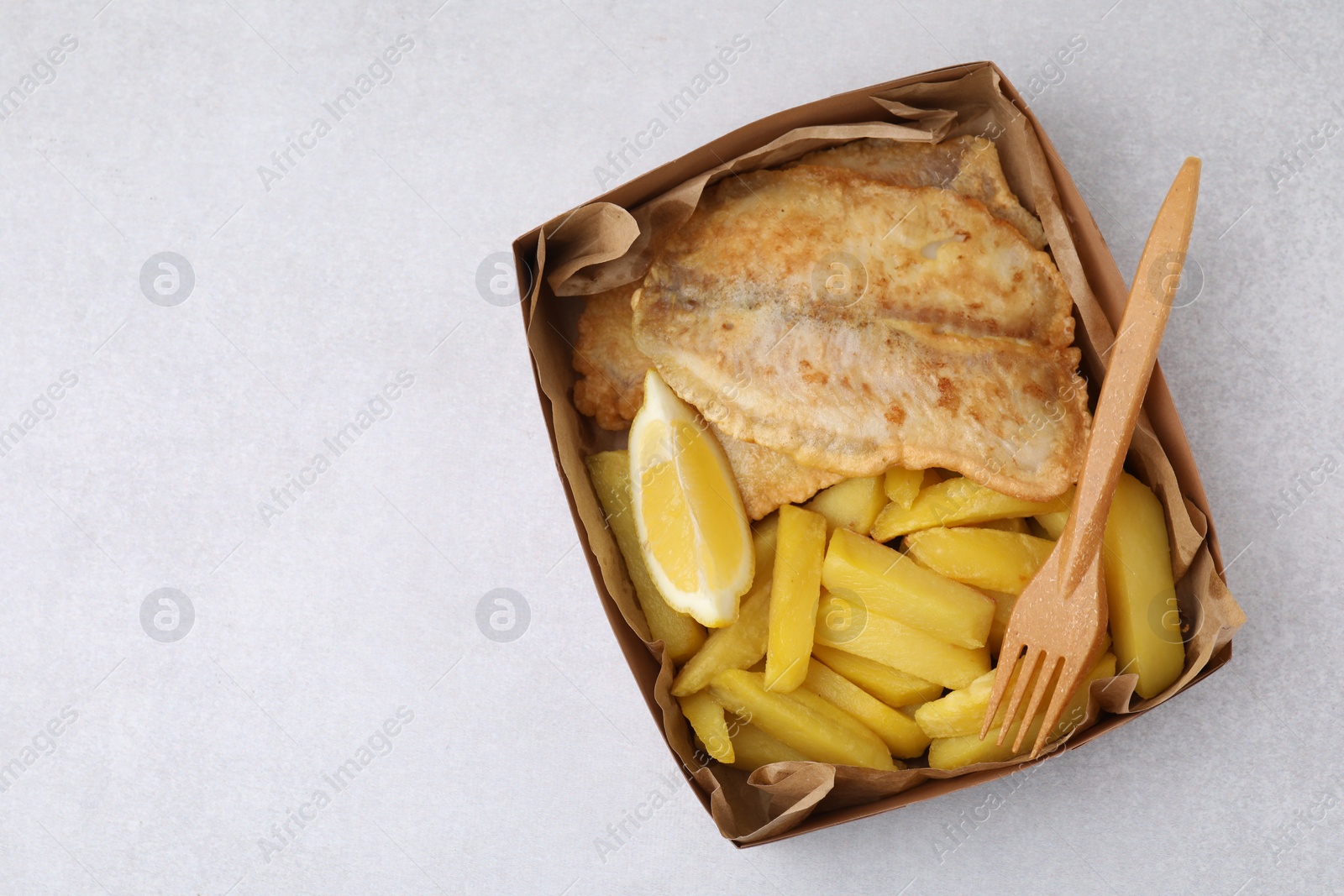 Photo of Delicious fish and chips in paper box served on light gray table, top view. Space for text