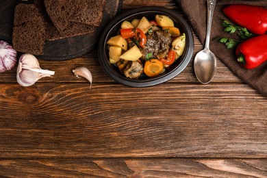 Photo of Tasty cooked dish with potatoes in earthenware served on wooden table, flat lay. Space for text