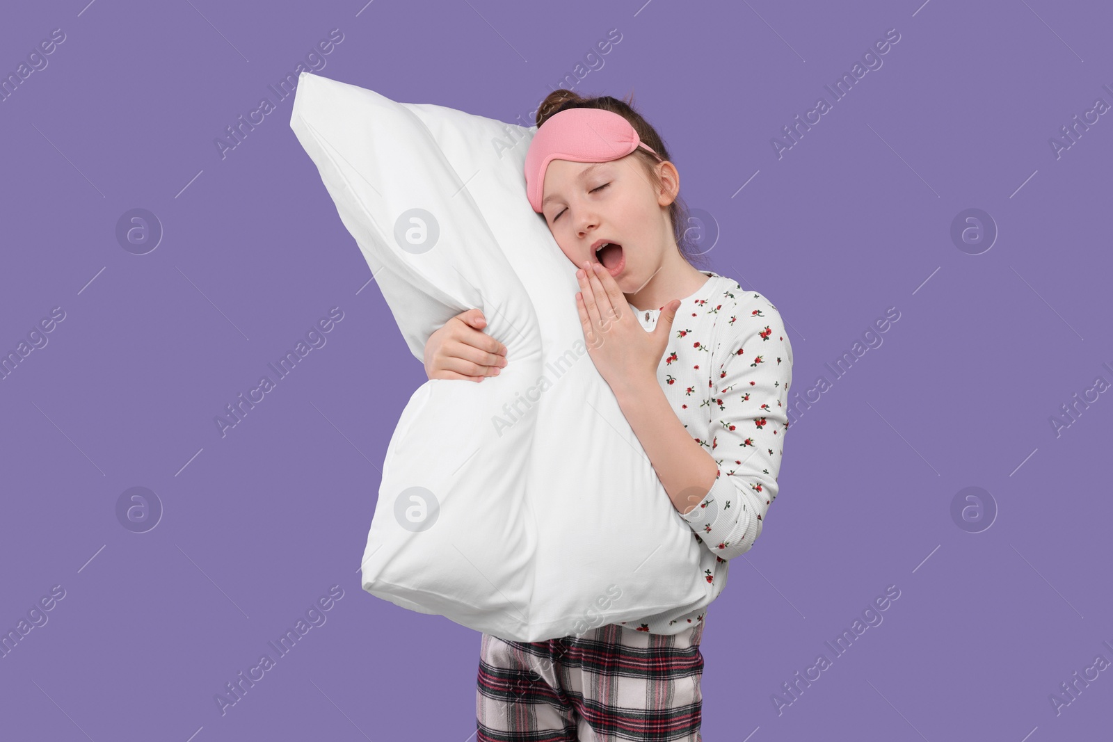 Photo of Girl with sleep mask and pillow yawning on purple background. Insomnia problem