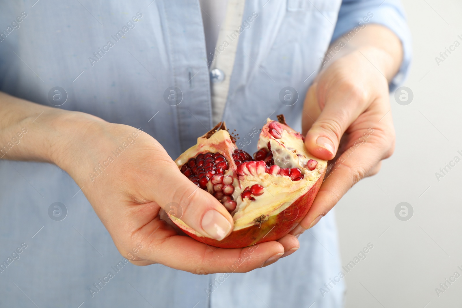 Photo of Woman holding ripe pomegranate on light background, closeup