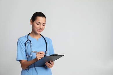 Photo of Portrait of young medical assistant with stethoscope and clipboard on color background. Space for text