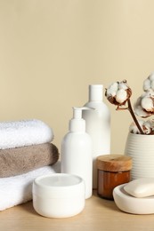 Photo of Different bath accessories and cotton flower on wooden table against beige background