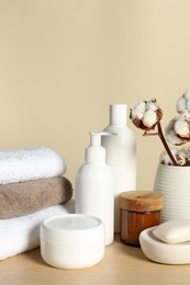 Different bath accessories and cotton flower on wooden table against beige background