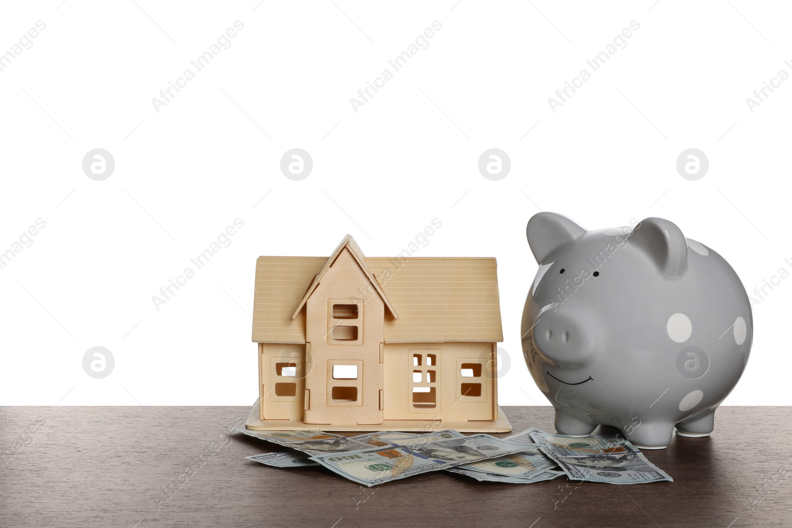 Photo of Piggy bank, house model and dollar banknotes on wooden table against white background. Saving money concept