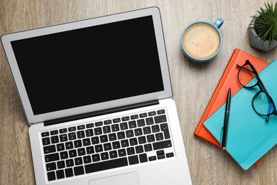 Modern laptop, cup of coffee and office stationery on wooden table, flat lay. Distance learning