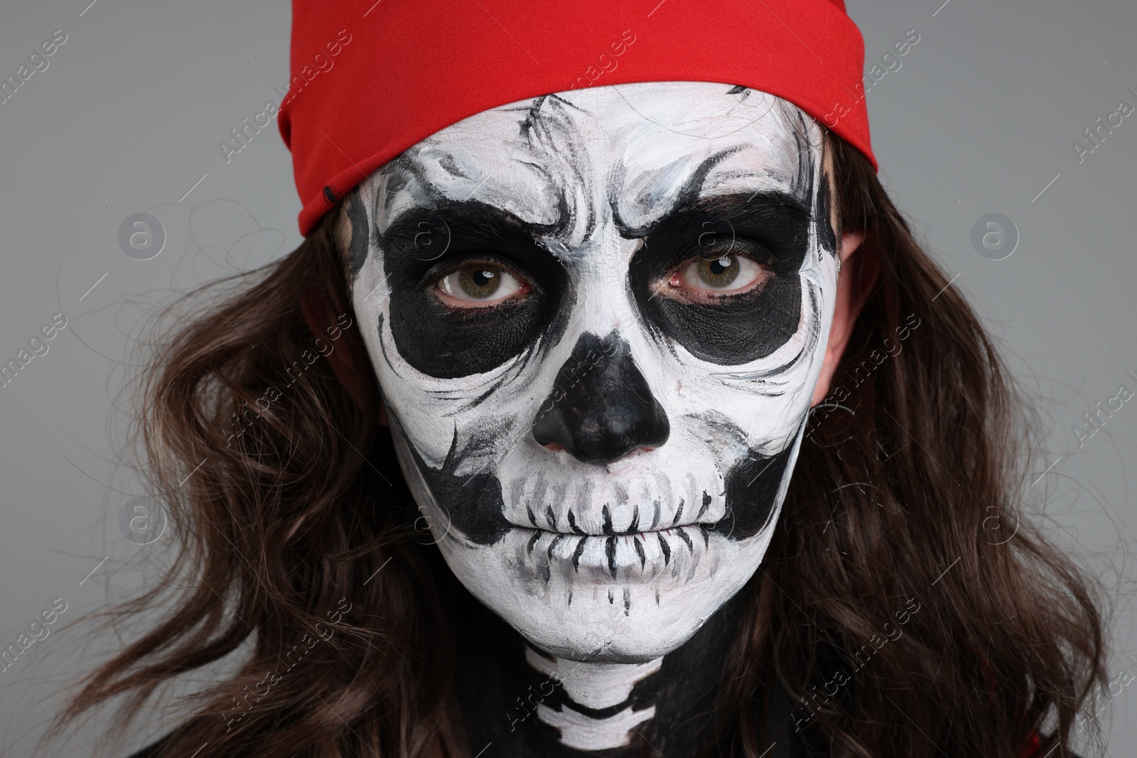 Photo of Man with skull makeup and red bandana on light grey background, closeup. Halloween celebration