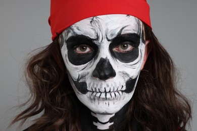 Photo of Man with skull makeup and red bandana on light grey background, closeup. Halloween celebration