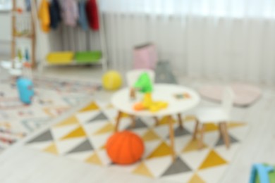 Photo of Blurred view of child`s playroom with different toys and furniture. Stylish kindergarten interior