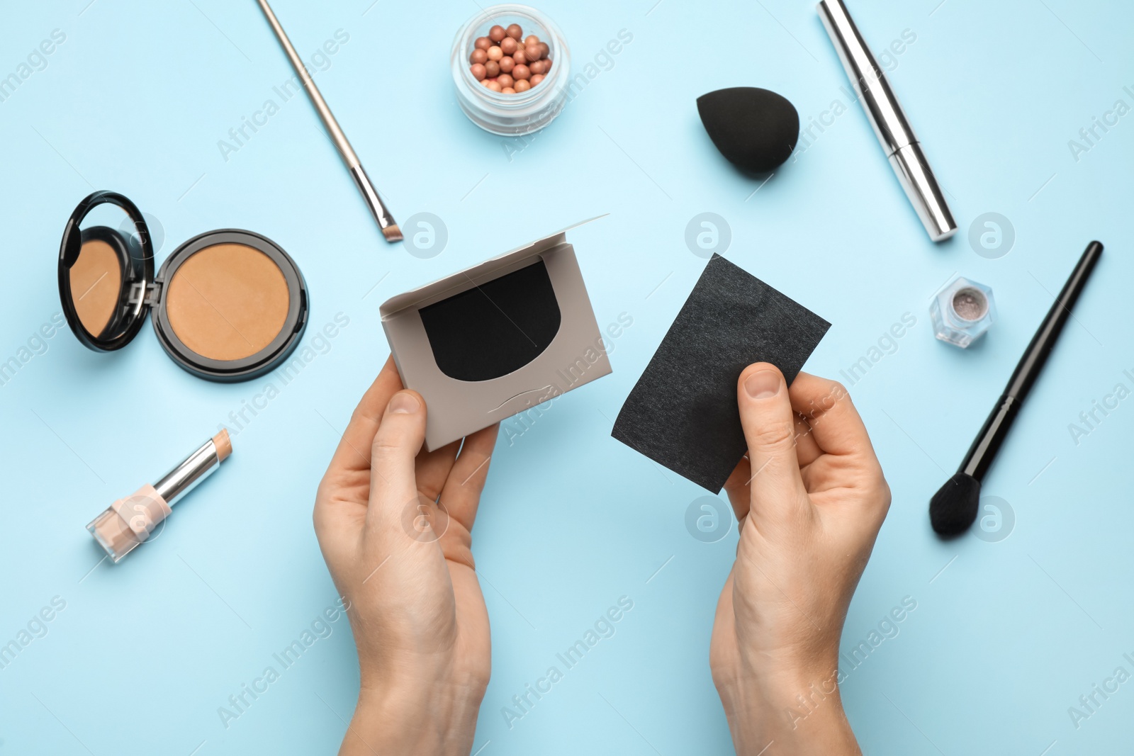 Photo of Woman with package of oil blotting tissues and decorative cosmetics on light blue background, top view. Mattifying wipes