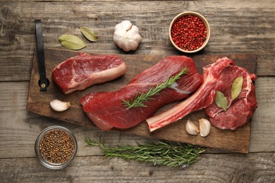 Photo of Pieces of raw beef meat and spices on wooden table, flat lay