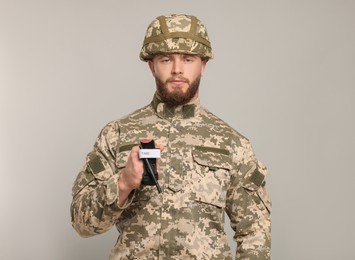 Photo of Soldier in military uniform holding medical tourniquet on light grey background. Space for text