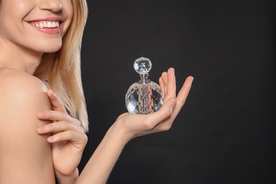 Photo of Young woman with bottle of perfume on black background, closeup