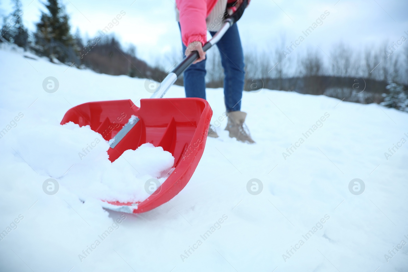 Photo of Woman cleaning snow with shovel outdoors on winter day, closeup