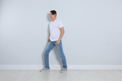 Young man in stylish jeans near light wall