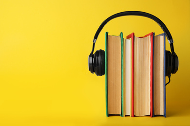 Photo of Books with modern headphones on yellow background. Space for text