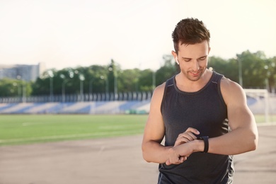 Photo of Young sportsman with wireless earphones and smart watch at stadium