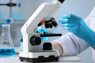 Scientist dripping sample onto Petri dish while working with microscope in laboratory, closeup