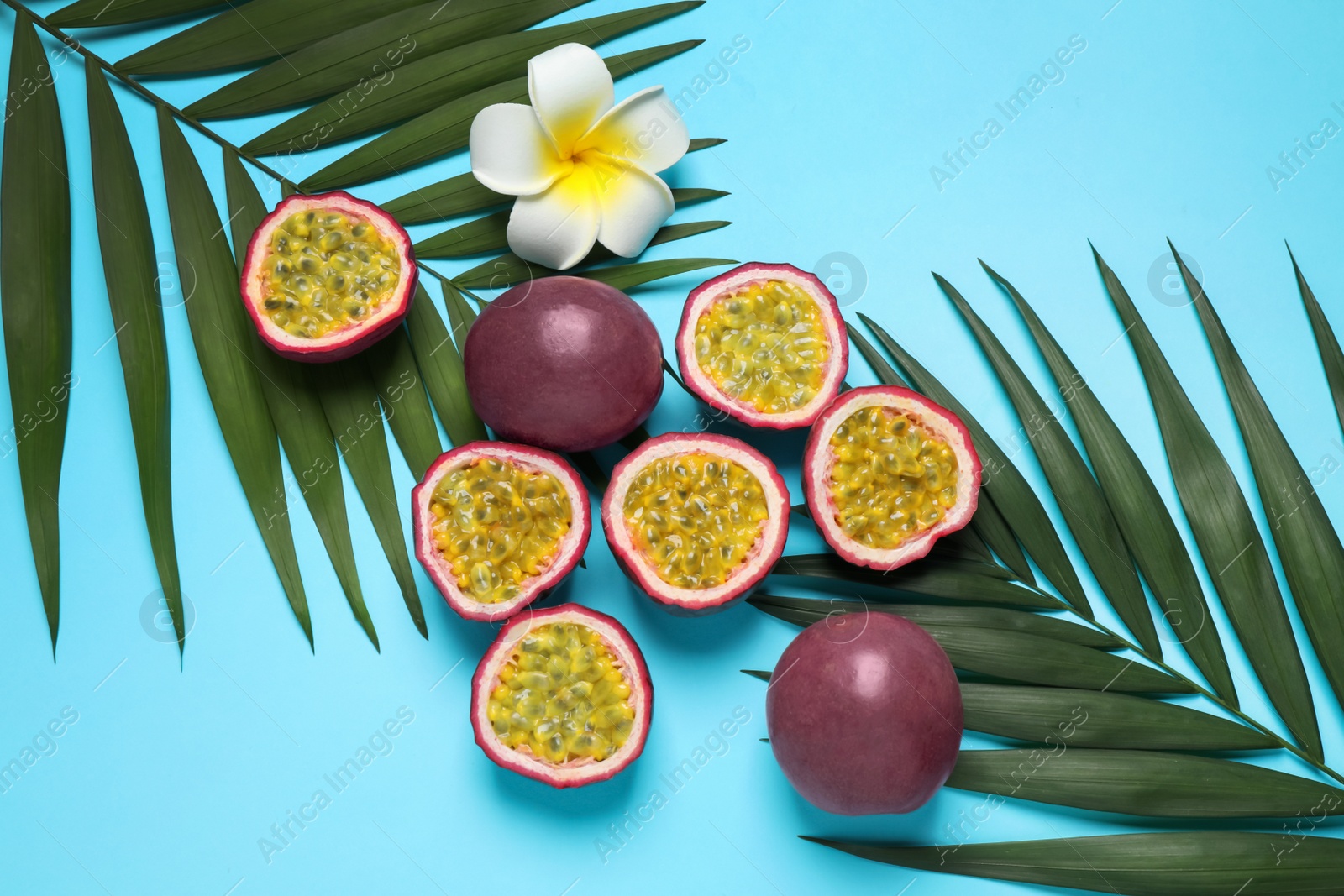 Photo of Passion fruits (maracuyas), flower and palm leaves on light blue background, flat lay