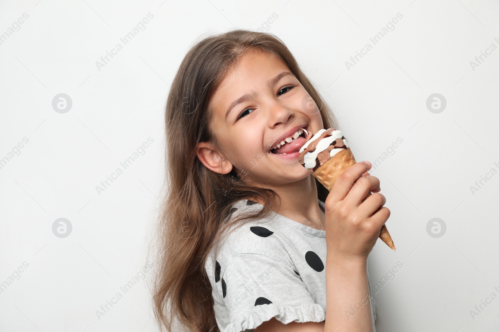 Photo of Adorable little girl with delicious ice cream against light background